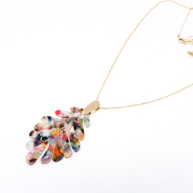 May include: A gold chain necklace with a multi-colored, abstract leaf-shaped pendant. The pendant is made of a translucent material with swirls of red, orange, yellow, green, blue, and purple.
