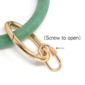 May include: A green glitter silicone key ring with a gold metal clasp. The clasp has a screw to open it.