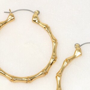 May include: A pair of gold bamboo hoop earrings. The earrings are made of a thick, textured metal that resembles bamboo.