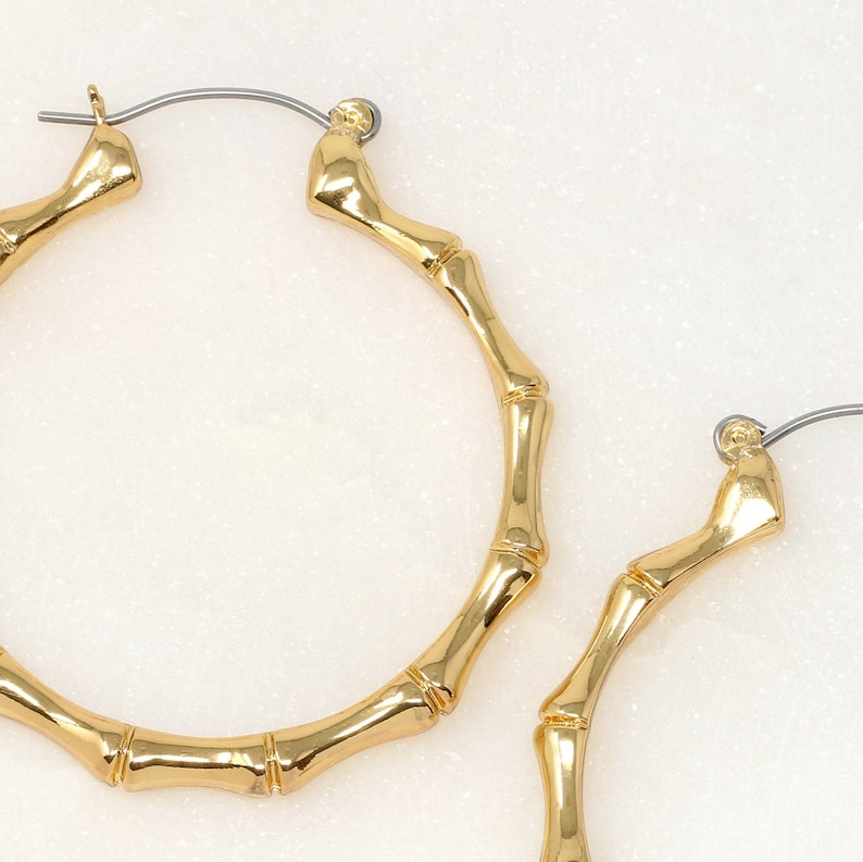 May include: A pair of gold bamboo hoop earrings. The earrings are made of a thick, textured metal that resembles bamboo.