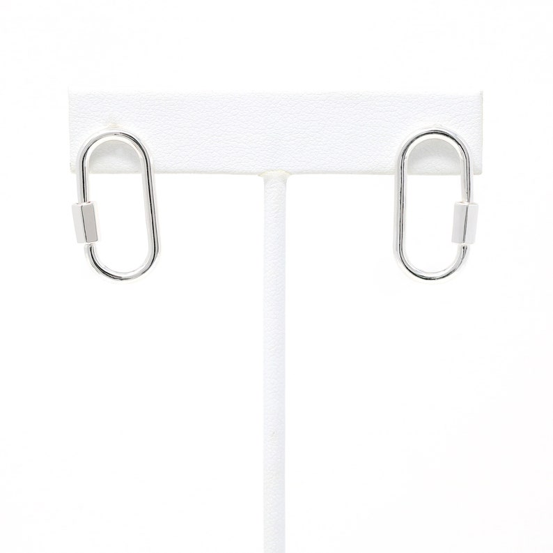 May include: A pair of silver oval-shaped earrings with a small silver bar on each earring.