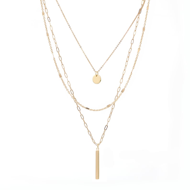 A set of 3 layered necklace in gold with a small disc and a skinny bar charms.