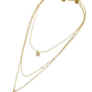 A three-layered gold necklace featuring a script initial charm and a small circle charm paved with stones.