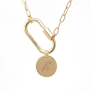 May include: A gold chain necklace with a gold carabiner clasp and a round gold pendant with the letter "E" engraved on it.