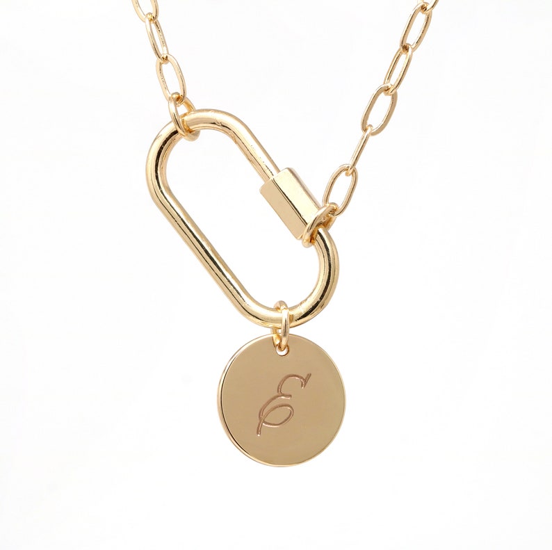 May include: A gold chain necklace with a gold carabiner clasp and a round gold pendant with the letter "E" engraved on it.