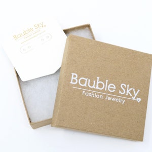 May include: A brown cardboard box with a white logo that says "Bauble Sky Fashion Jewelry". The box is open and the inside is lined with white tissue paper.
