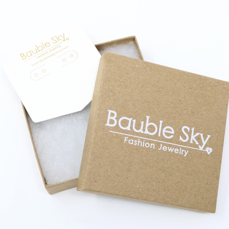 May include: A brown cardboard box with a white logo that says "Bauble Sky Fashion Jewelry". The box is open and the inside is lined with white tissue paper.