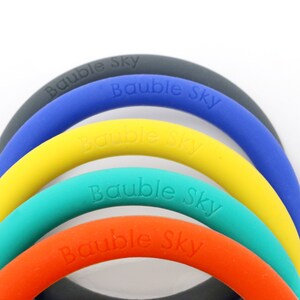 May include: Five colorful silicone rings with the words "Bauble Sky" embossed on each ring. The rings are stacked on top of each other, with the gray ring on the bottom and the blue ring on the top.