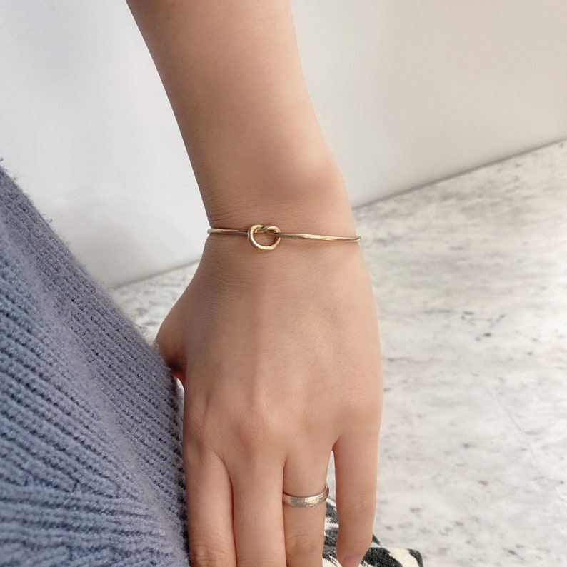 Wrist wearing the thin gold loop knot cuff bracelet, resting on a marble countertop.