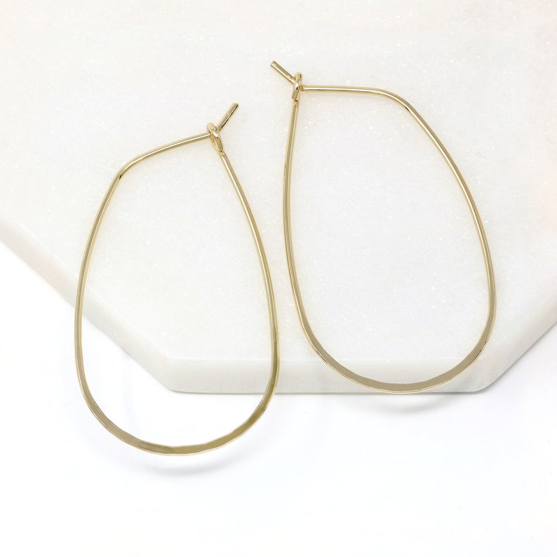 K&ouml;nnte beinhalten: Ein Paar goldene Ohrringe in Tropfenform. Die Ohrringe sind aus d&uuml;nnem, geh&auml;mmertem Metall gefertigt und haben ein schlichtes, elegantes Design.