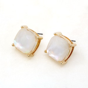 May include: A pair of square stud earrings. Each earring has a pearlescent, iridescent, square-shaped stone set in a gold-coloured metal frame. The earrings have a post backing.