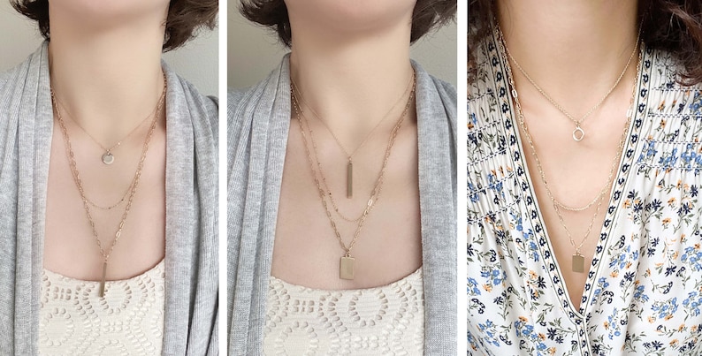 May include: Three gold necklaces with different pendant styles, including a circle, a bar, and a square. The necklaces are layered on a person's neck.