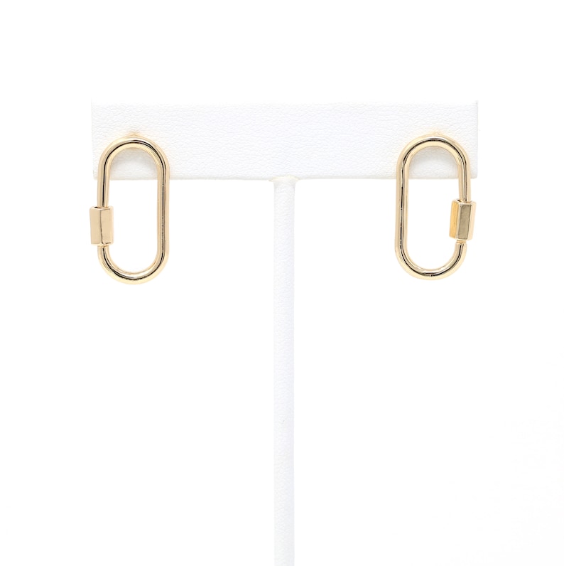 May include: A pair of gold oval-shaped earrings with a small gold bar on each earring.
