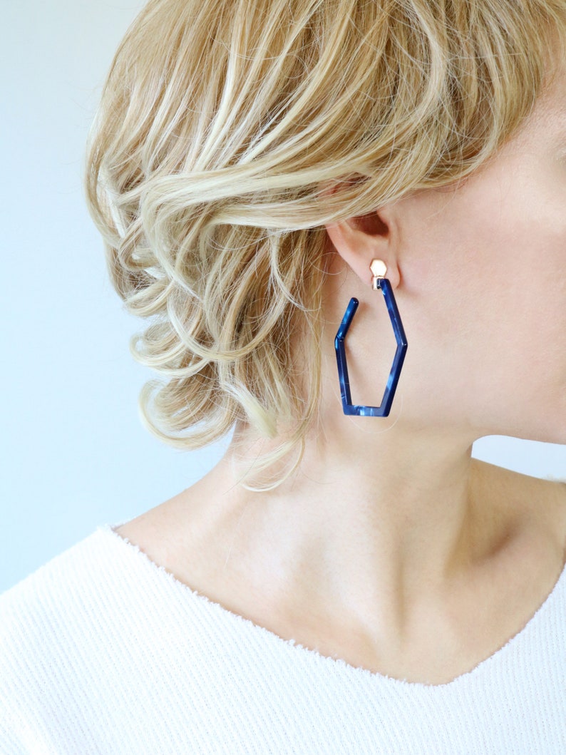 May include: A pair of blue geometric hoop earrings. The earrings are made of a dark blue plastic material and have a hexagonal shape.