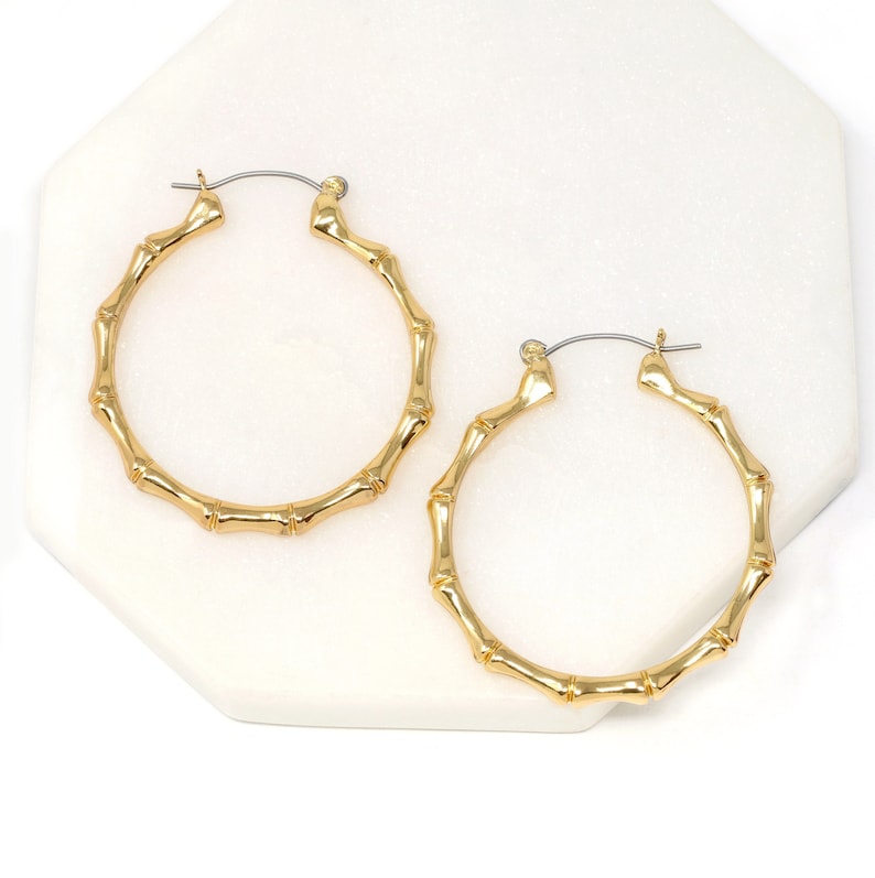 May include: A pair of gold bamboo hoop earrings. The earrings are made of a thick, textured metal that resembles bamboo.
