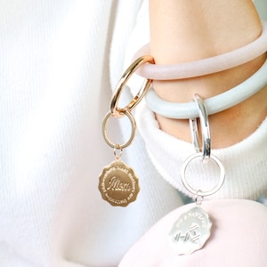 May include: Two gold and silver keychains with charms. The gold charm has the word "Mom" and the text "Philosophers have lost much sleep over the question of whether we are getting better or worse." The silver charm has the text "Fit & Fabulin" and a dumbbell graphic.