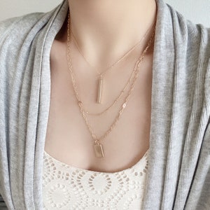 Wearing a modern triple-layered necklace in gold dangled with two bar charms.