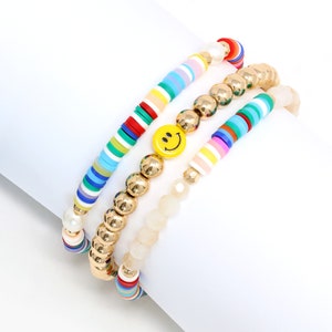 May include: A set of three colorful beaded bracelets. One bracelet features a smiley face charm, another has gold beads, and the third has white and multi-colored beads.
