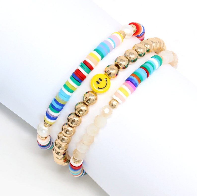 May include: A set of three colorful beaded bracelets. One bracelet features a smiley face charm, another has gold beads, and the third has white and multi-colored beads.