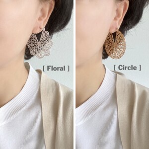 May include: Two pairs of earrings are shown. One is silver-colored and floral-shaped, the other is gold-colored and oval-shaped. The text "Floral" and "Circle" are below each earring, respectively. The earrings are worn by a person wearing a white shirt and a beige cardigan.