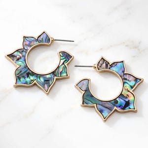 May include: A pair of gold-toned hoop earrings featuring a scalloped, flower-like outer edge inlaid with iridescent abalone shell. The earrings have a circular center cutout and a standard post-back closure for secure attachment to the earlobe.