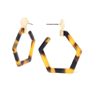 May include: A pair of gold and tortoiseshell hexagon hoop earrings. The earrings are made of a lightweight material and have a simple, elegant design.