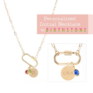 May include: Gold chain necklace with a carabiner clasp and a charm with the letter "R" and two birthstones. The charm is attached to a smaller round charm with the word "CRA" engraved on it.  Personalized Initial Necklace w/ Birthstone.