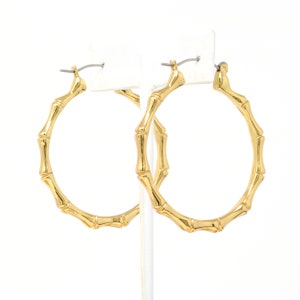 May include: A pair of gold bamboo hoop earrings. The earrings are large and have a simple design.