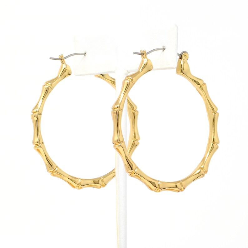 May include: A pair of gold bamboo hoop earrings. The earrings are large and have a simple design.