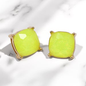 A pair of square, cushion-cut stud earrings featuring bright neon yellow glass stones with fine glitter inside. The stones are set in a shiny gold-toned four-prong metal setting.