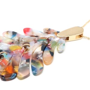 May include: A multi-colored, abstract, resin pendant necklace with a gold chain and a gold clasp. The pendant is made of several layers of resin, each with a different pattern and color.