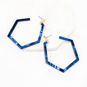 May include: A pair of blue hexagonal hoop earrings with a marbled pattern. The earrings have a gold-toned post.