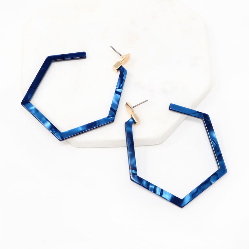 May include: A pair of blue hexagonal hoop earrings with a marbled pattern. The earrings have a gold-toned post.