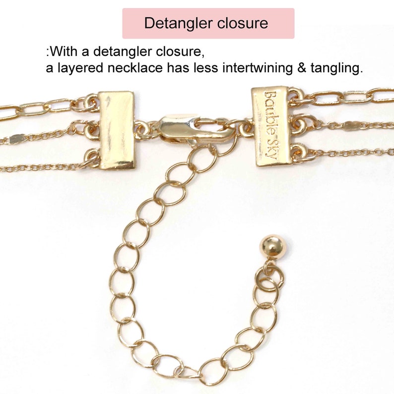 May include: Gold layered necklace with a detangler closure. The closure features a small, round bead and a rectangular tag that says "Bauble Sky".