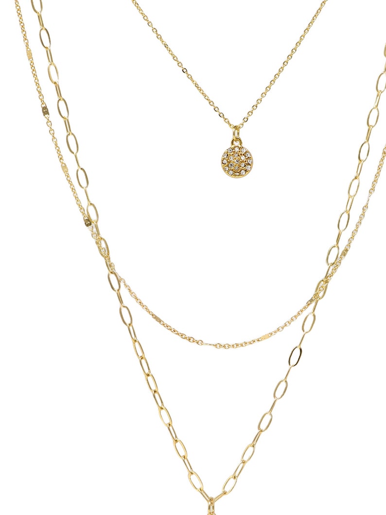 A three-layered gold necklace featuring a script initial charm and a small circle charm paved with stones.