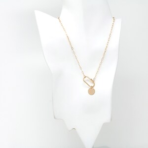 May include: A gold chain necklace with a gold circle pendant and a gold clasp. The necklace is on a white mannequin.