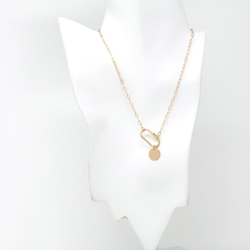 May include: A gold chain necklace with a gold circle pendant and a gold clasp. The necklace is on a white mannequin.