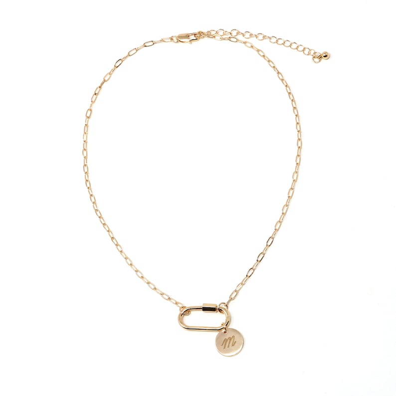 May include: A gold chain necklace with a gold carabiner clasp and a small gold disc charm with the letter "M" engraved on it.