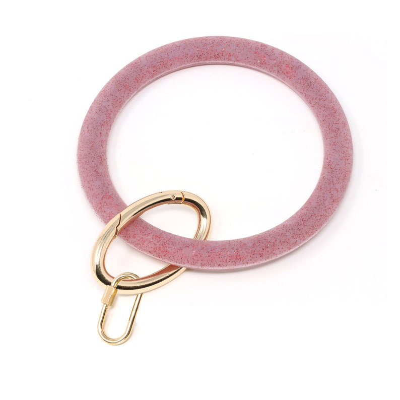 May include: A pink glitter key ring with a gold metal clasp. The ring is made of a soft, flexible material.
