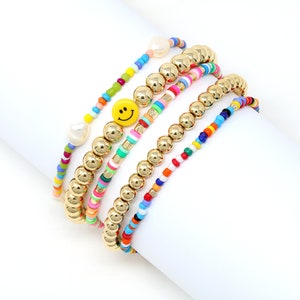 May include: Set of five colorful beaded bracelets with gold beads and a yellow smiley face charm. The bracelets feature a variety of colors, including red, orange, yellow, green, blue, and purple.