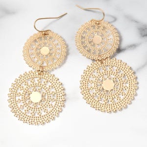 May include: A pair of gold-colored, filigree earrings. Each earring features two circular, openwork designs connected by a small chain. The earrings have a hook closure and a small, solid circle in the center of each filigree circle.