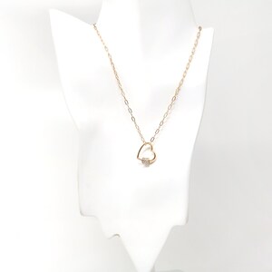 May include: A gold chain necklace with a heart-shaped pendant featuring a small clear stone.