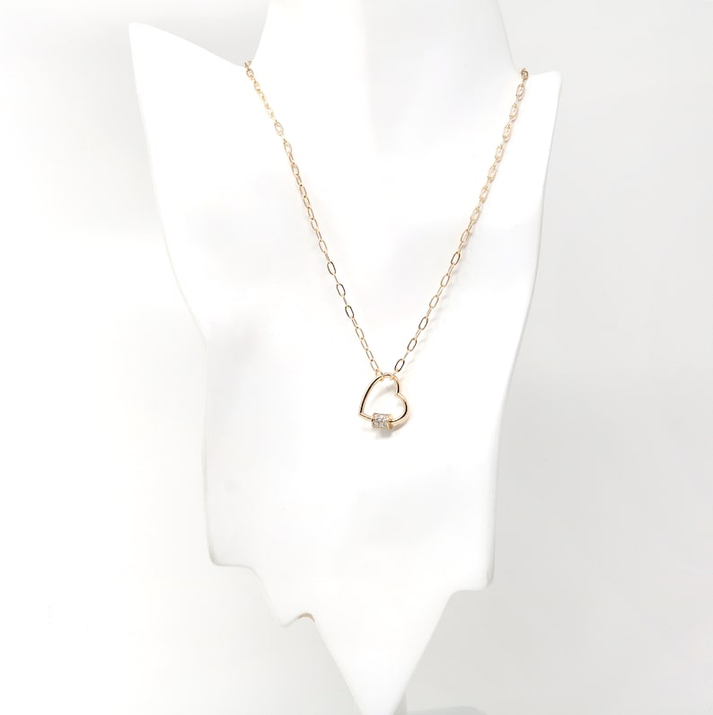 May include: A gold chain necklace with a heart-shaped pendant featuring a small clear stone.