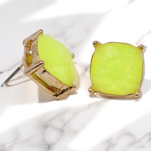 A pair of square, cushion-cut stud earrings featuring bright neon yellow glass stones with fine glitter inside. The stones are set in a shiny gold-toned four-prong metal setting.
