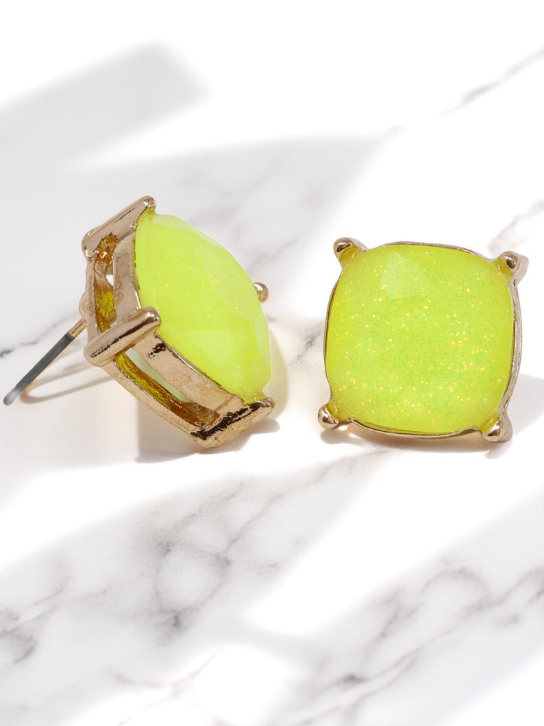 A pair of square, cushion-cut stud earrings featuring bright neon yellow glass stones with fine glitter inside. The stones are set in a shiny gold-toned four-prong metal setting.