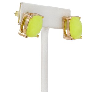 A pair of square, cushion-cut stud earrings featuring bright neon yellow glass stones with fine glitter inside. The stones are set in a shiny gold-toned four-prong metal setting.
