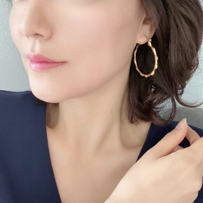May include: Gold hoop earrings with a bamboo-like design. The earrings are large and circular.