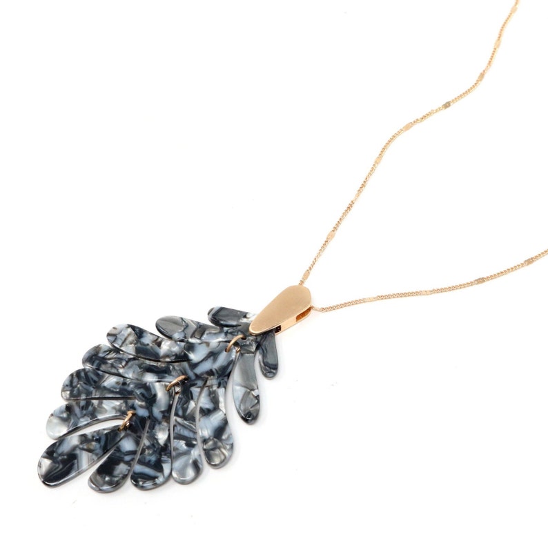 May include: A gold chain necklace with a black and white marbled leaf pendant.