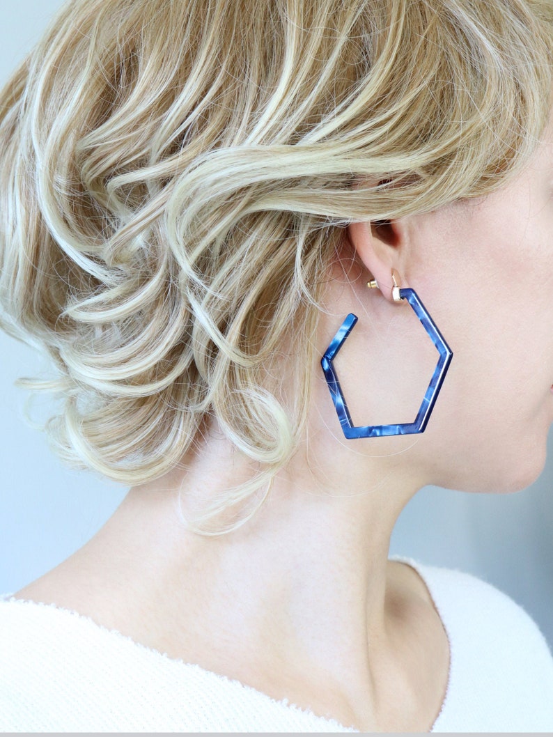 May include: A pair of blue hexagonal hoop earrings. The earrings are made of a translucent material with a marbled pattern.