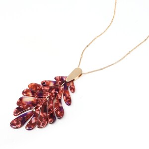 May include: A gold chain necklace with a large, red and purple leaf-shaped pendant. The pendant is made of a marbled material.